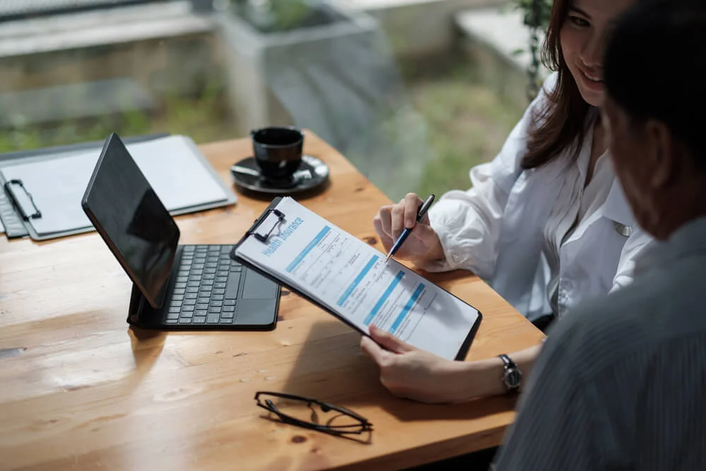 Female health insurance broker presenting his insurance benefits to businessman fill out insurance policy.