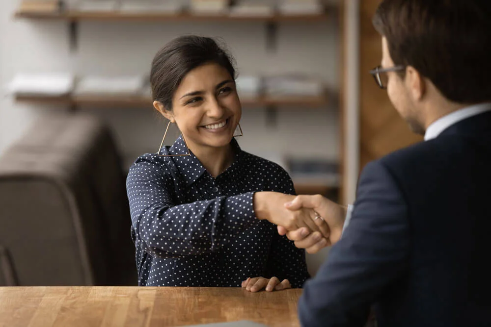 Greetings, you are hired. Happy young indian female successful job seeker shake hand of male hr manager being accepted on vacant place